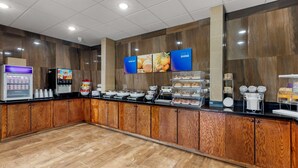 Un área de desayuno autoservicio con diversas opciones de alimentos, una máquina de café y un mostrador refrigerado.