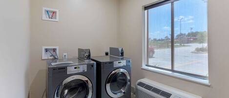A laundry room with two front-loading washers and dryers, a window with a view of a parking lot, and a wall-mounted air conditioner.