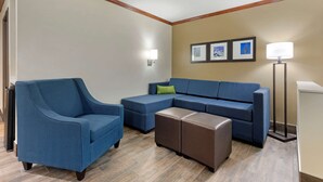 Una sala de estar con un sofá azul, un sillón azul y un otoman marrón. Hay tres cuadros enmarcados en la pared y una lámpara de pie.