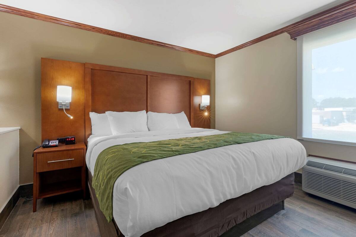 A hotel room with a large bed, wooden headboard, bedside lamps, a nightstand, and a window with a view.