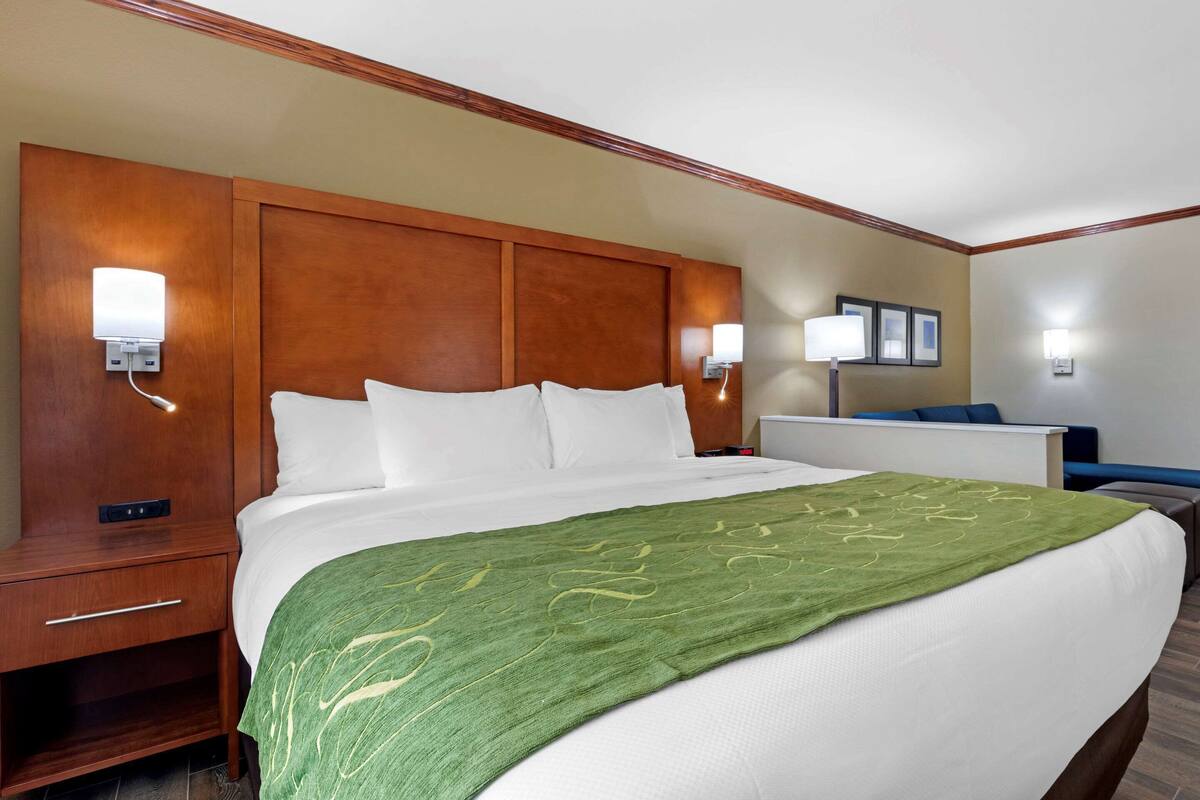 A hotel room with a large bed, wooden headboard, two bedside tables, and wall-mounted lamps.
