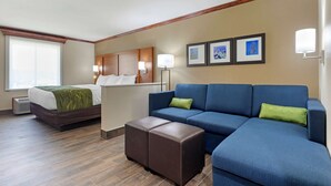 Una habitación de hotel con cama, sofá, una mesita y televisión instalada en la pared.