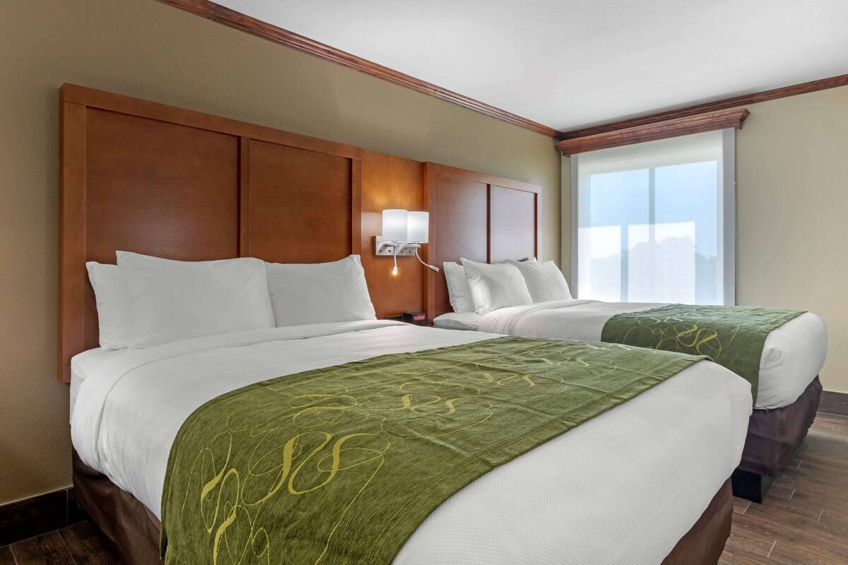 A hotel room with two beds, a large window, and a wooden headboard.