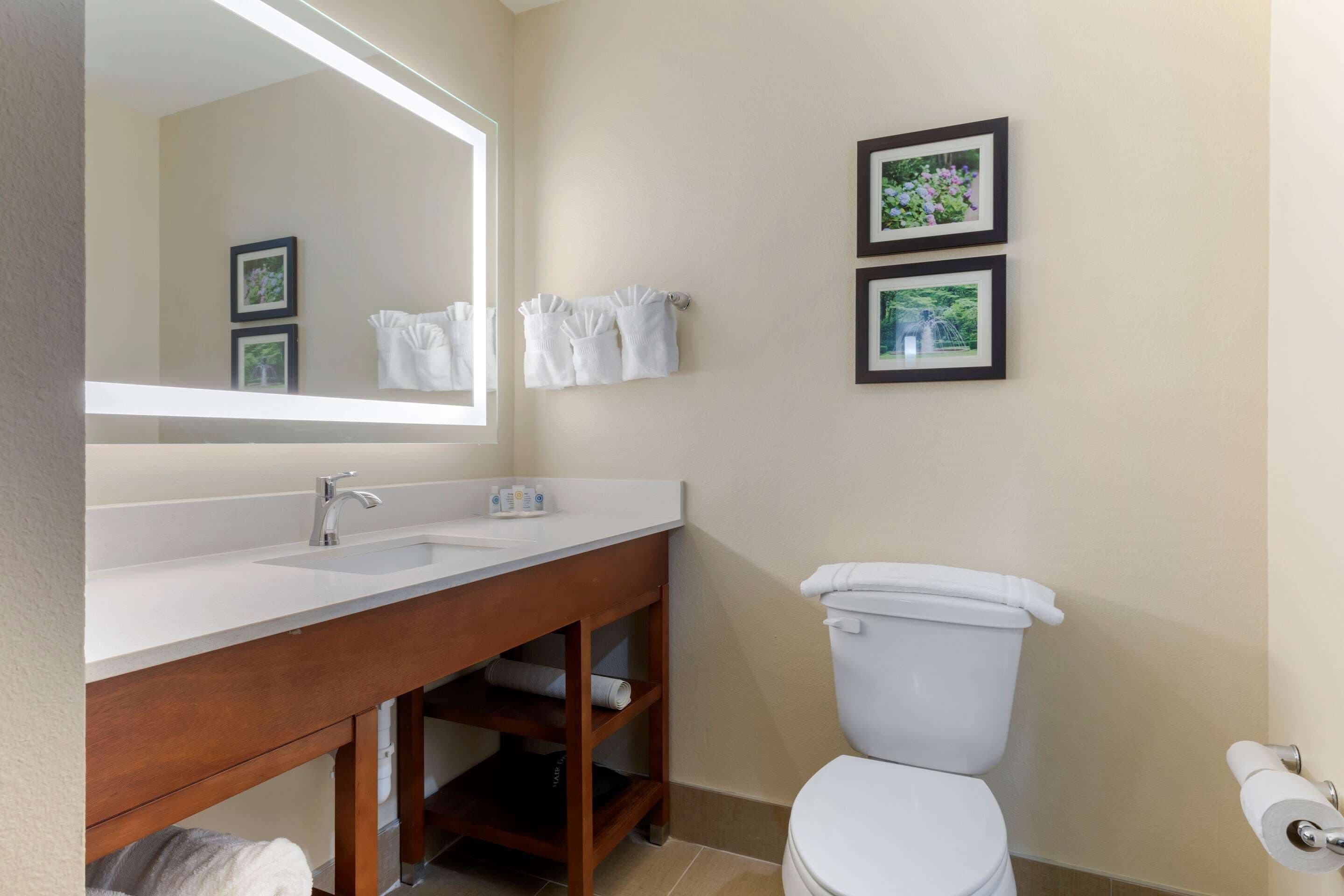 A bathroom with a white sink, mirror, and toilet. There are two framed pictures on the wall and towels hanging on a rack.