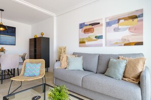 Uma sala de estar moderna com um sofá cinzento, uma cadeira de vime e arte abstrata nas paredes.