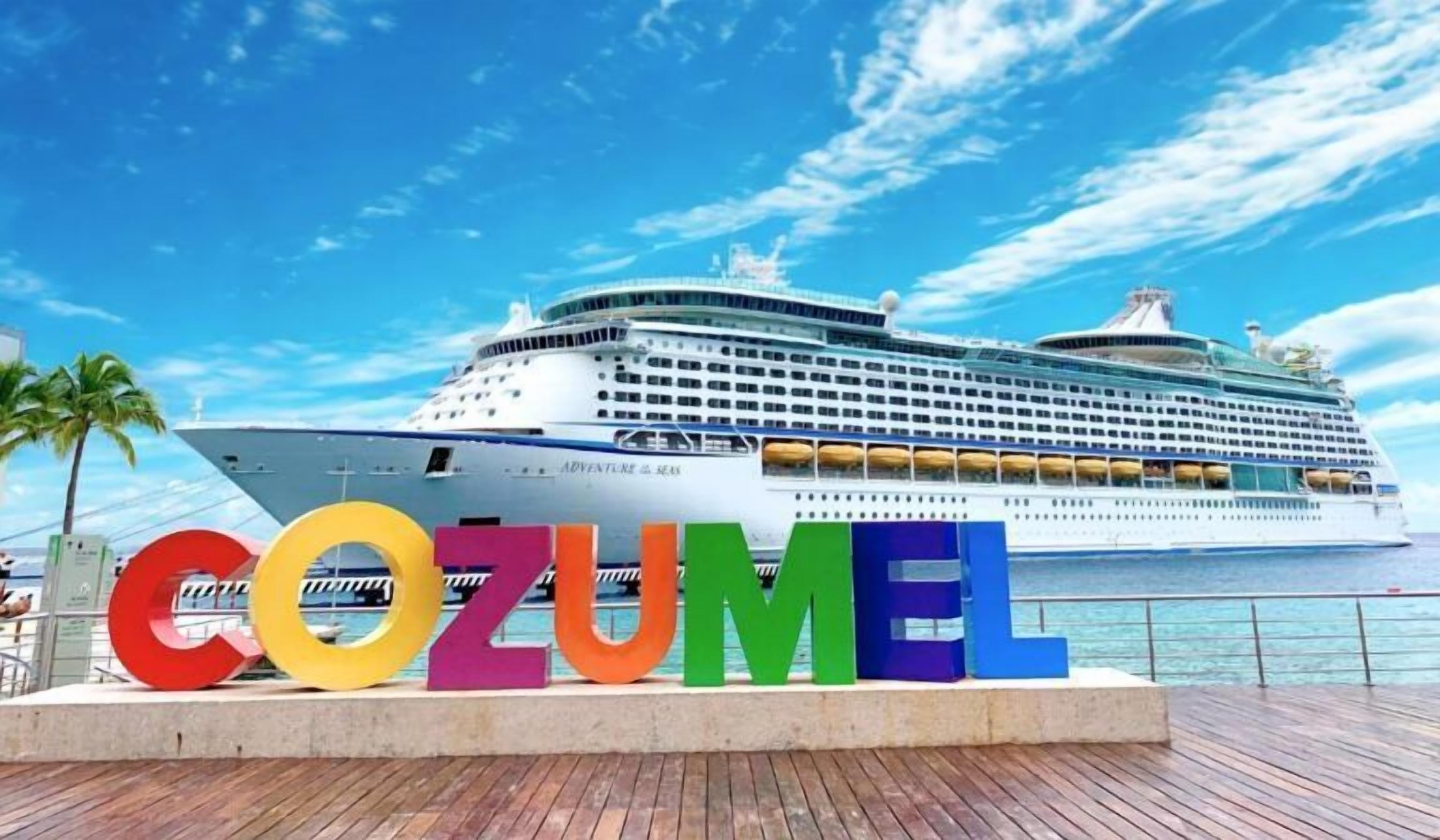 A large cruise ship named 'Adventure of the Seas' docked at a port with the word 'COZUMEL' displayed prominently in colorful letters.