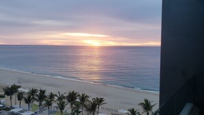Une vue sur la plage au coucher du soleil, avec des palmiers et des parasols de plage.