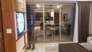 Un salon comprenant un téléviseur, un canapé, une table basse et une porte-fenêtre coulissante donnant sur une cuisine et un coin repas.