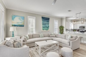 A modern living room with a sectional sofa, a white coffee table, and a kitchen area with a microwave and cabinets.