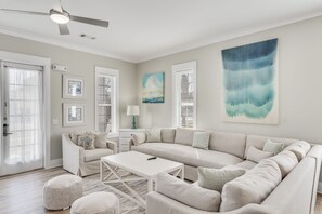 A modern living room with a beige sofa, a white coffee table, and a ceiling fan.
