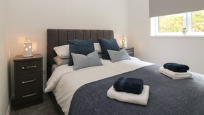 A neatly made bed with a grey and white duvet, multiple pillows, and two bedside lamps. - Ocean View (Banff)