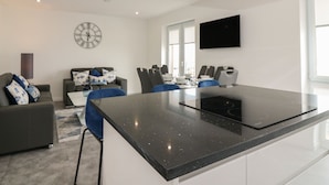A modern kitchen with a central island, a dining area with chairs, a sofa, and a TV mounted on the wall. - Ocean View (Banff)