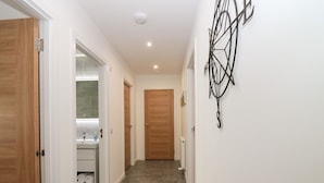 A hallway with a wooden door, a bathroom with a mirror and sink, and a decorative wall piece. - Ocean View (Banff)