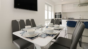 A modern dining area with a white table set for four, black chairs, and a flat-screen TV mounted on the wall. - Ocean View (Banff)