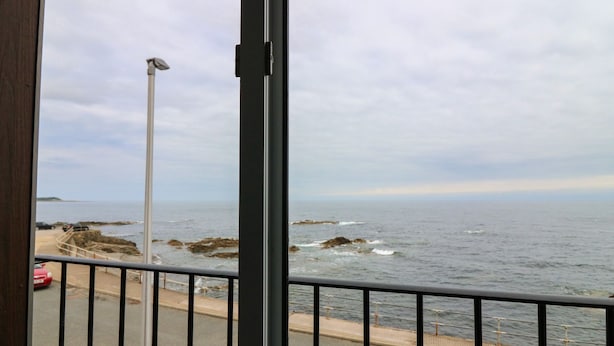 A coastal view from a balcony with a metal railing, a paved walkway, and a rocky shoreline. - Ocean View (Banff)