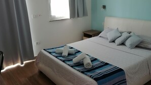 Hotellihuone, jossa on sänky, ikkuna verhoilla, yöpöytä ja pieni sivupöytä.