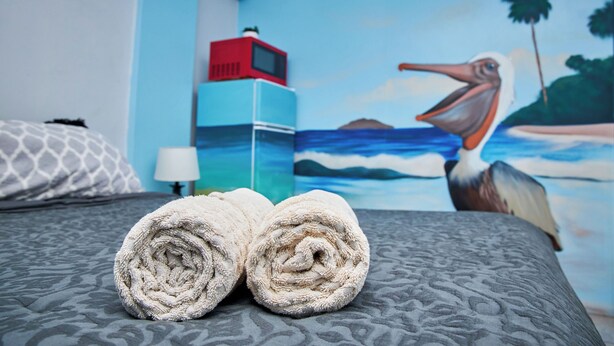 Una cama con toallas enrolladas, un microondas rojo y un cuadro de una playa con un pelícano.