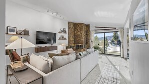 Un salon moderne avec un mur d’accent en pierre, un grand téléviseur à écran plat et un canapé agrémenté de coussins.