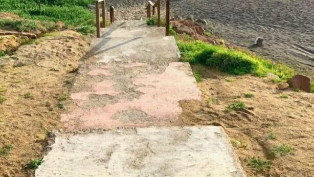 Ein Betonweg führt zu einer grünen Mülltonne.