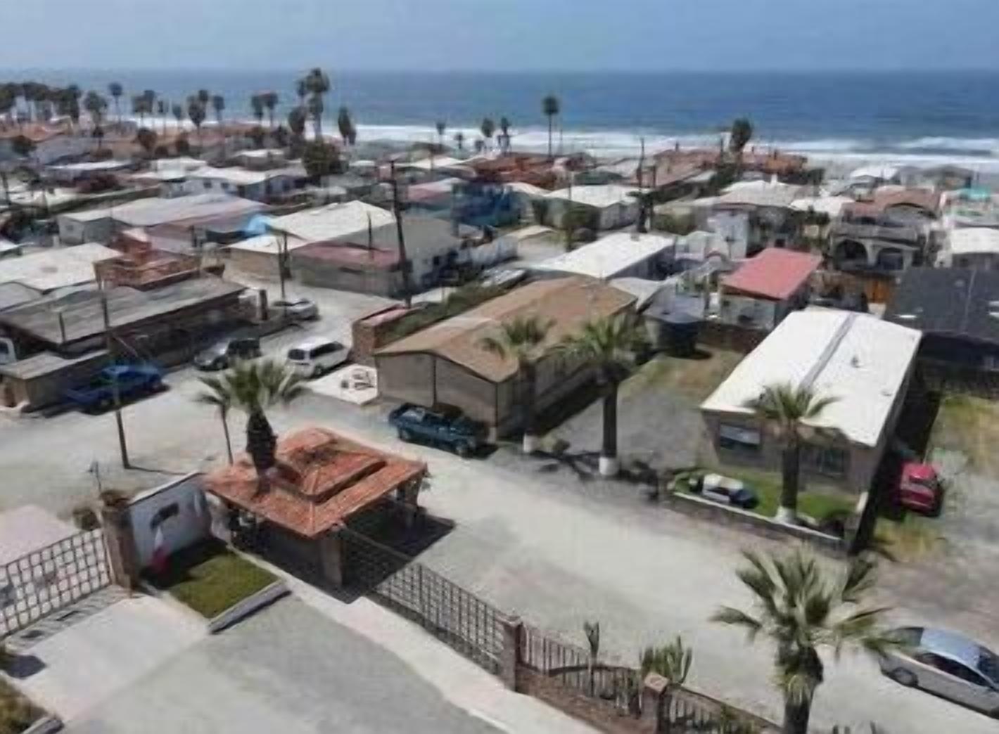 An aerial view of a coastal residential area with houses, some with red roofs, and a clear view of the ocean.