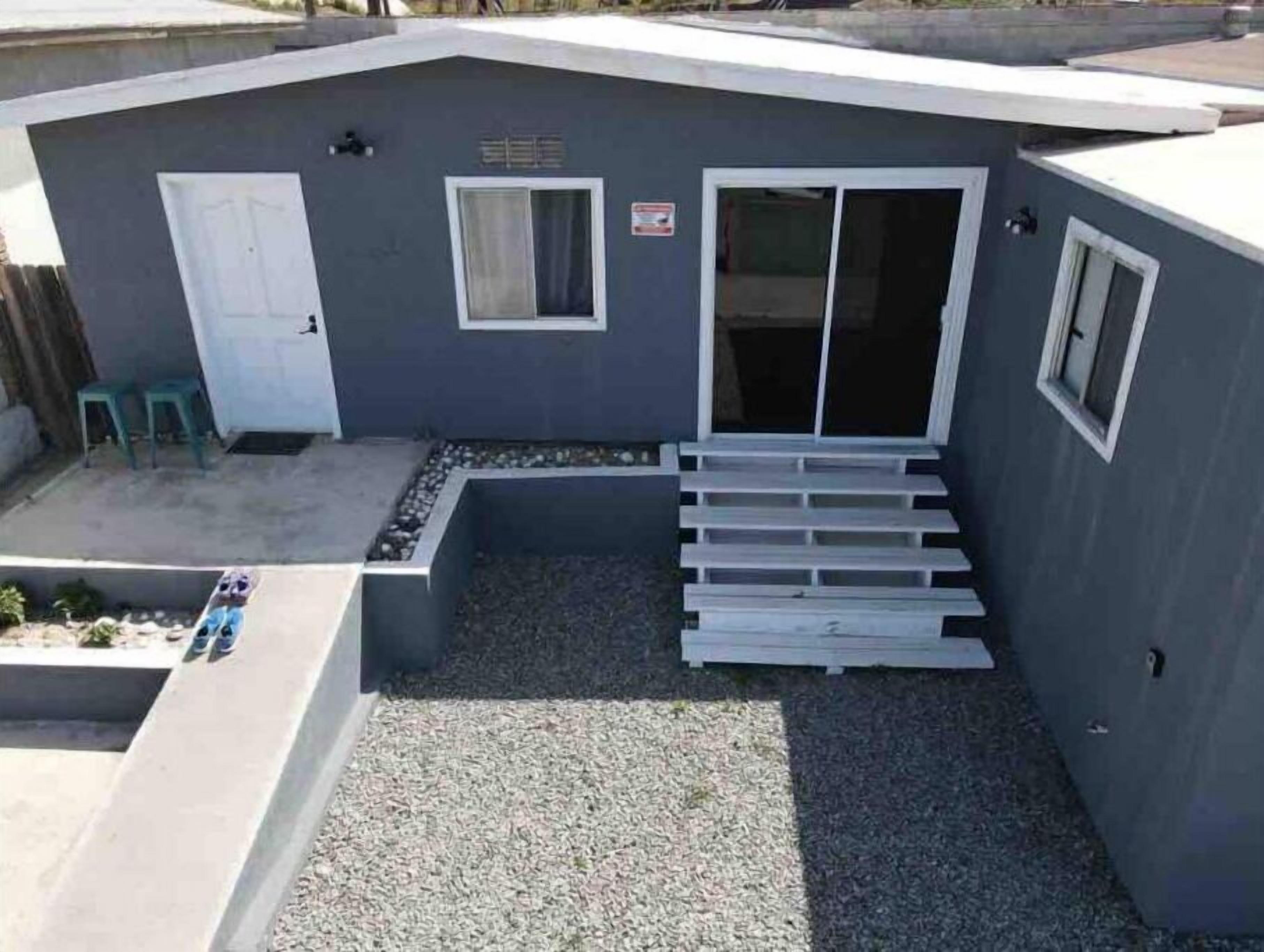 Un petit bâtiment d’un seul étage, à l’extérieur gris, avec une porte blanche et une fenêtre.