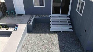Ein kleines, eingeschossiges Gebäude mit grauem Anstrich, einer weißen Tür und einem Fenster.