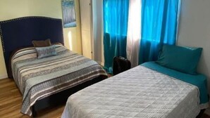 Una camera d'albergo con due letti, pavimento in legno e tende blu.