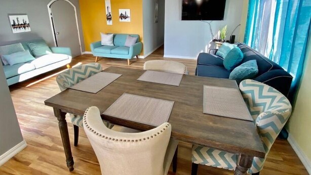 Un soggiorno moderno con un tavolo da pranzo in legno, due divani e una TV a parete.