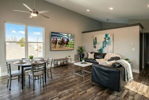 A modern living room with a dining area, a large window, a ceiling fan, and a mounted television. - Modern Loft+Sky Deck~Walk to Bourbon & Beyond (Louisville)
