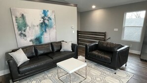 Un salon avec un canapé en cuir foncé, une table basse blanche et un tapis à motifs.
