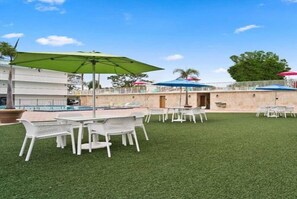 Ein Terrassenbereich im Freien mit weißen Plastiktischen und -stühlen, einem Pool und Sonnenschirmen.