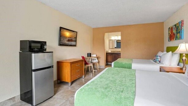 A hotel room with a bed, a desk, a refrigerator, and a painting on the wall. - Royal Park Orlando Timeless 2 DBL Beds Room with Pool (Kissimmee)