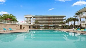 Une piscine entourée de chaises longues et de parasols, elle-même bordée d’un immeuble à plusieurs étages doté de balcons.