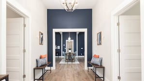 A hallway with a dark blue accent wall, wooden flooring, and a dining area in the background. - Charming Modern Farm House-5 min from Sport Center (Rock Hill)