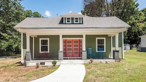 A single-story house with a green exterior, a red front door, and two blue chairs on the porch. - Charming Modern Farm House-5 min from Sport Center (Rock Hill)