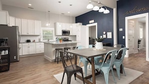 A modern kitchen with white cabinets, a central island with stools, and a dining table with chairs. - Charming Modern Farm House-5 min from Sport Center (Rock Hill)