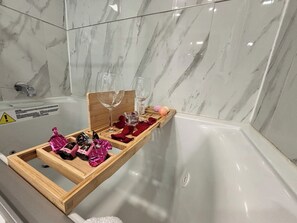 Une salle de bain avec un mur en marbre, un plateau en bois contenant des bouteilles et des verres, et un panneau d’avertissement.