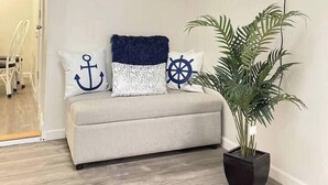 Ein Wohnzimmer mit einer Couch, marineblauen Kissen, einem an der Wand befestigten Fernseher und einem Topf mit einer Pflanze.