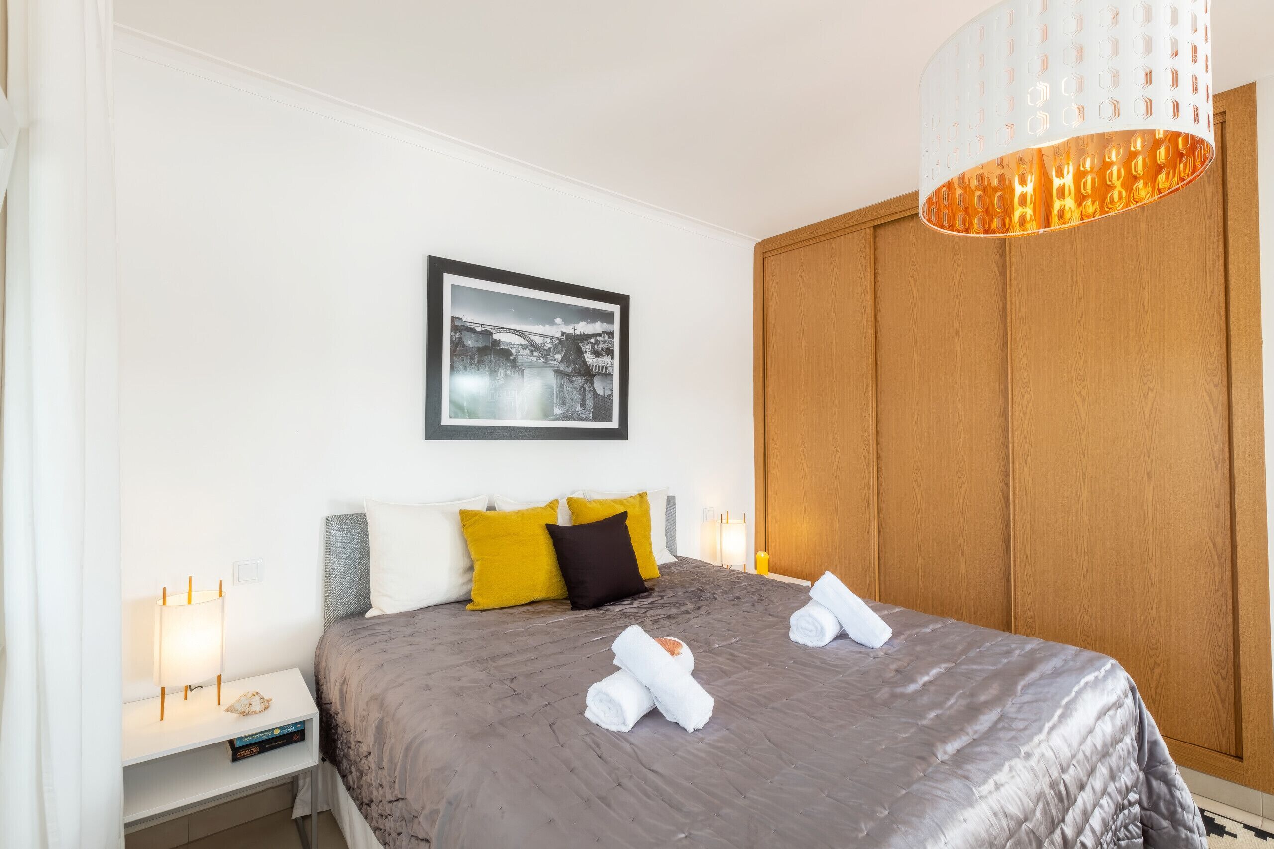 Hotellihuone, jossa on sänky, yöpöytä, seinällä oleva kehystetty kuva ja puinen vaatekaappi.