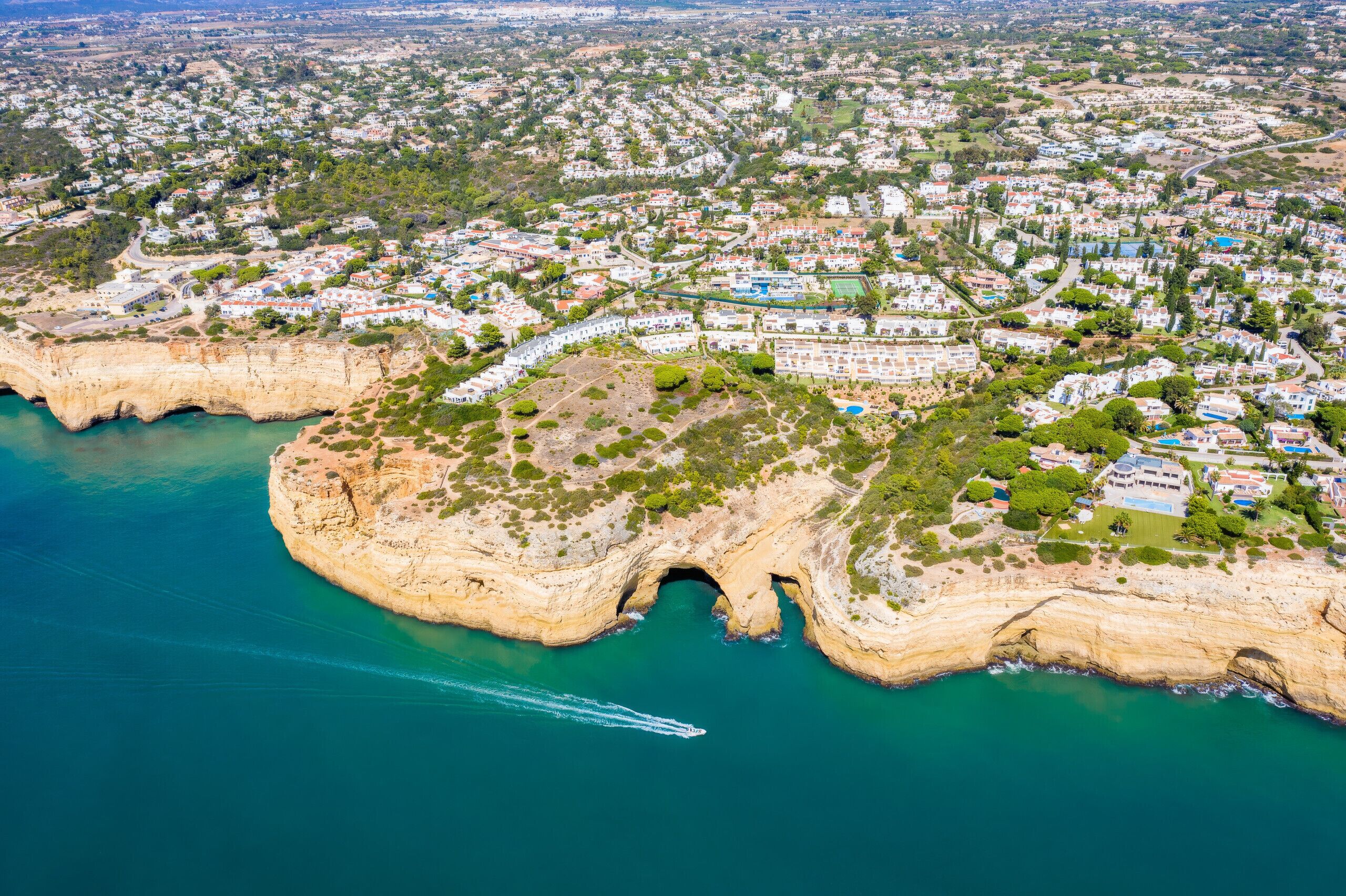 Vue aérienne d’une ville côtière avec des immeubles résidentiels, une falaise imposante et une mer bleue et limpide.