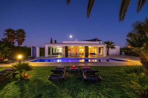 Een modern huis met een zwembad, terrasmeubels buiten en een goed verlicht terras.