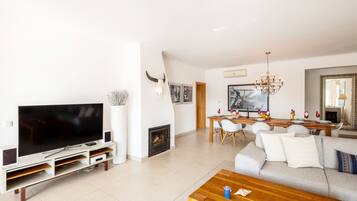 A modern living room with a flat-screen TV, a fireplace, a dining area with a wooden table, and a sofa.