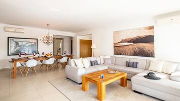 A modern living room with a dining area, a chandelier, and a large landscape painting.