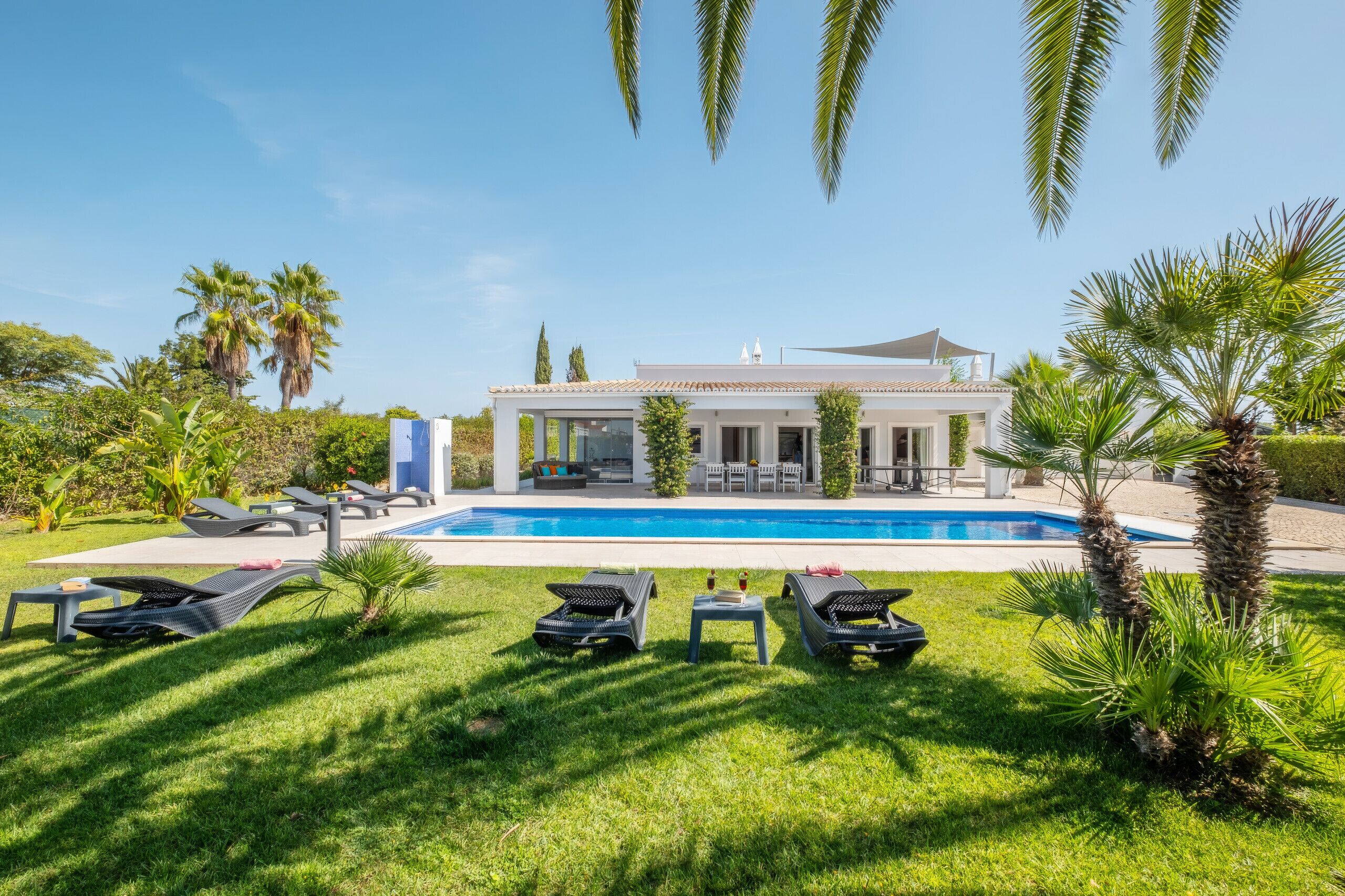 Une villa moderne dotée d’une piscine, de chaises longues et d’un jardin bien entretenu.