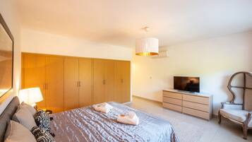 A bedroom with a large bed, wooden wardrobe, a television, and a chair.
