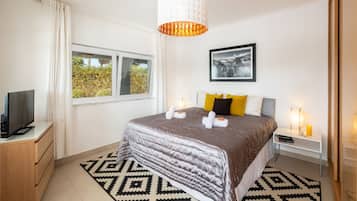 A hotel room with a bed, a television, a window with curtains, a picture on the wall, and a patterned rug.