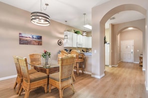 A dining area with wicker chairs, a glass table, pendant lighting, and a kitchen with white cabinets and a microwave. - Top Floor Bahama Bay Condo | 3BR/2BA | 2 Balconies | Near Disney (Davenport)