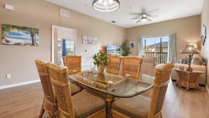 A spacious living room with a glass-top dining table surrounded by wicker chairs, a ceiling fan, and a view of the outdoors. - Top Floor Bahama Bay Condo | 3BR/2BA | 2 Balconies | Near Disney (Davenport)