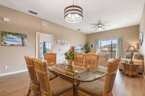 A spacious living room with a glass-top dining table surrounded by wicker chairs, a ceiling fan, and a view of the outdoors. - Top Floor Bahama Bay Condo | 3BR/2BA | 2 Balconies | Near Disney (Davenport)