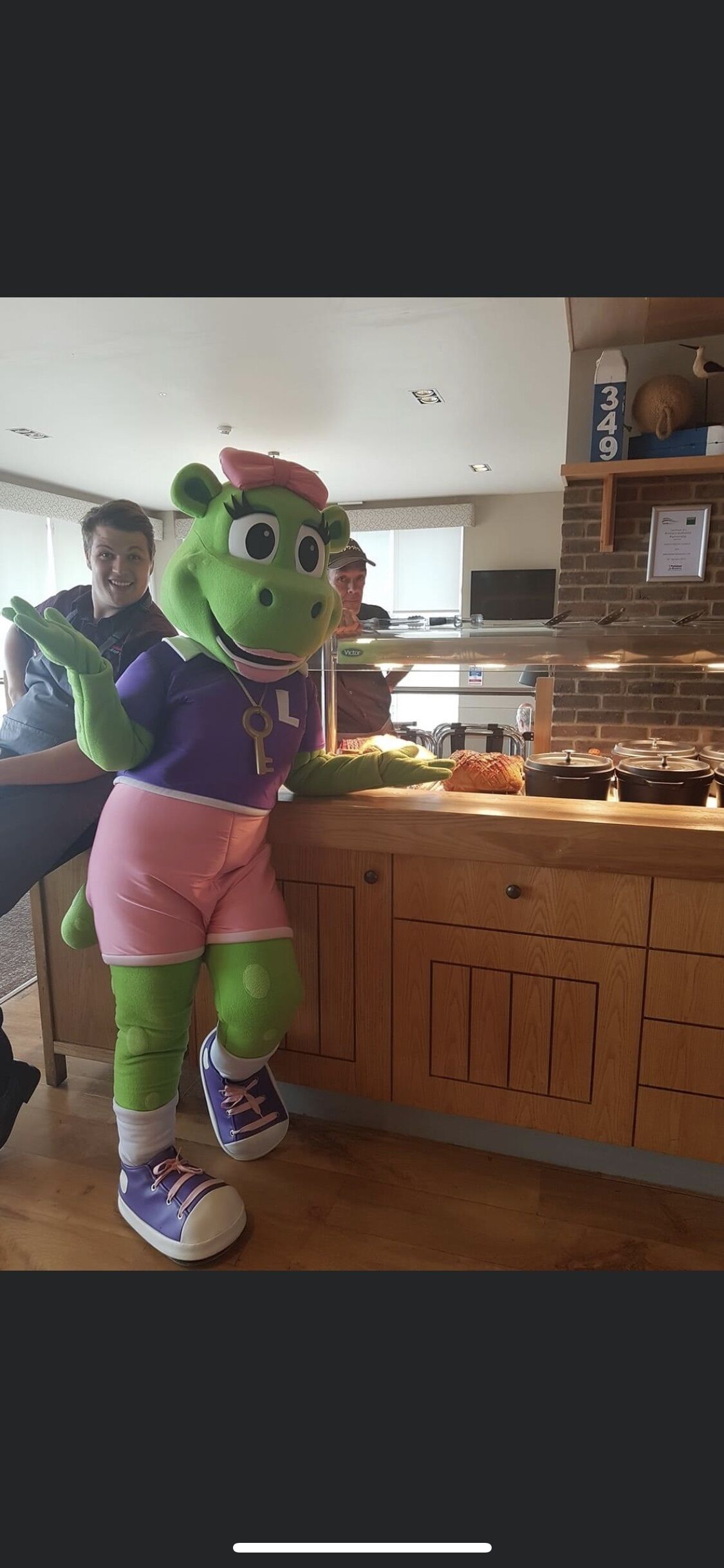 Un personaje con disfraz de mascota en un área de cocina con armarios de madera y una encimera.